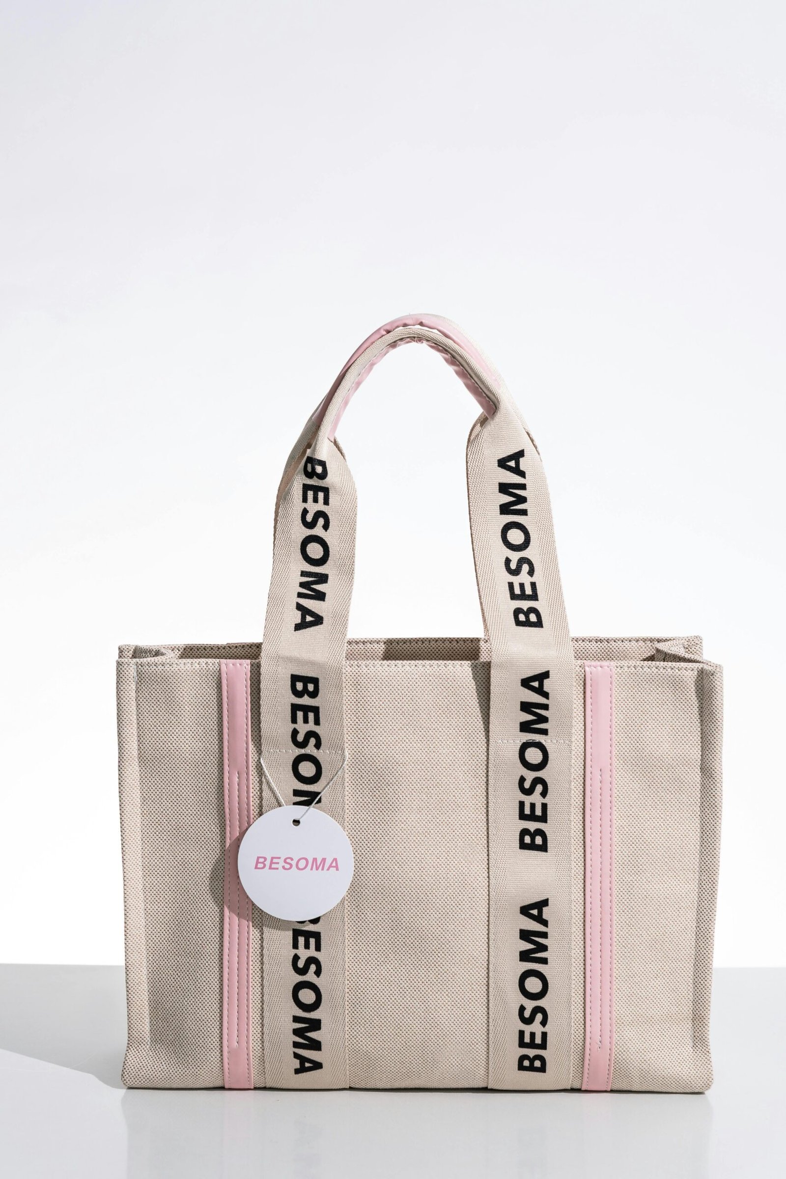 Fashionable beige canvas handbag with pink accents and branding. Perfect for stylish outings.